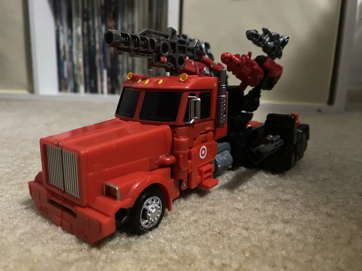 A red toy semi-truck with multiple mounted weapons is shown on a carpeted floor, with the word 'target' overlaid as text…