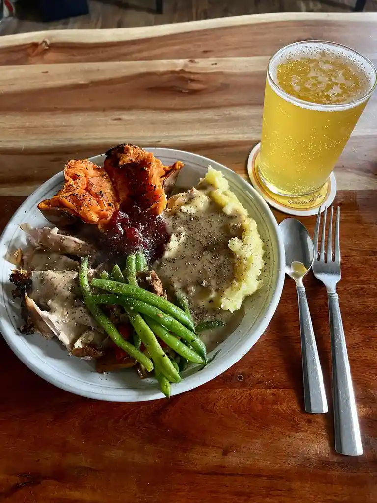 A plate of food including roasted sweet potato, mashed potatoes with gravy, green beans, and turkey meat sits on a wooden…