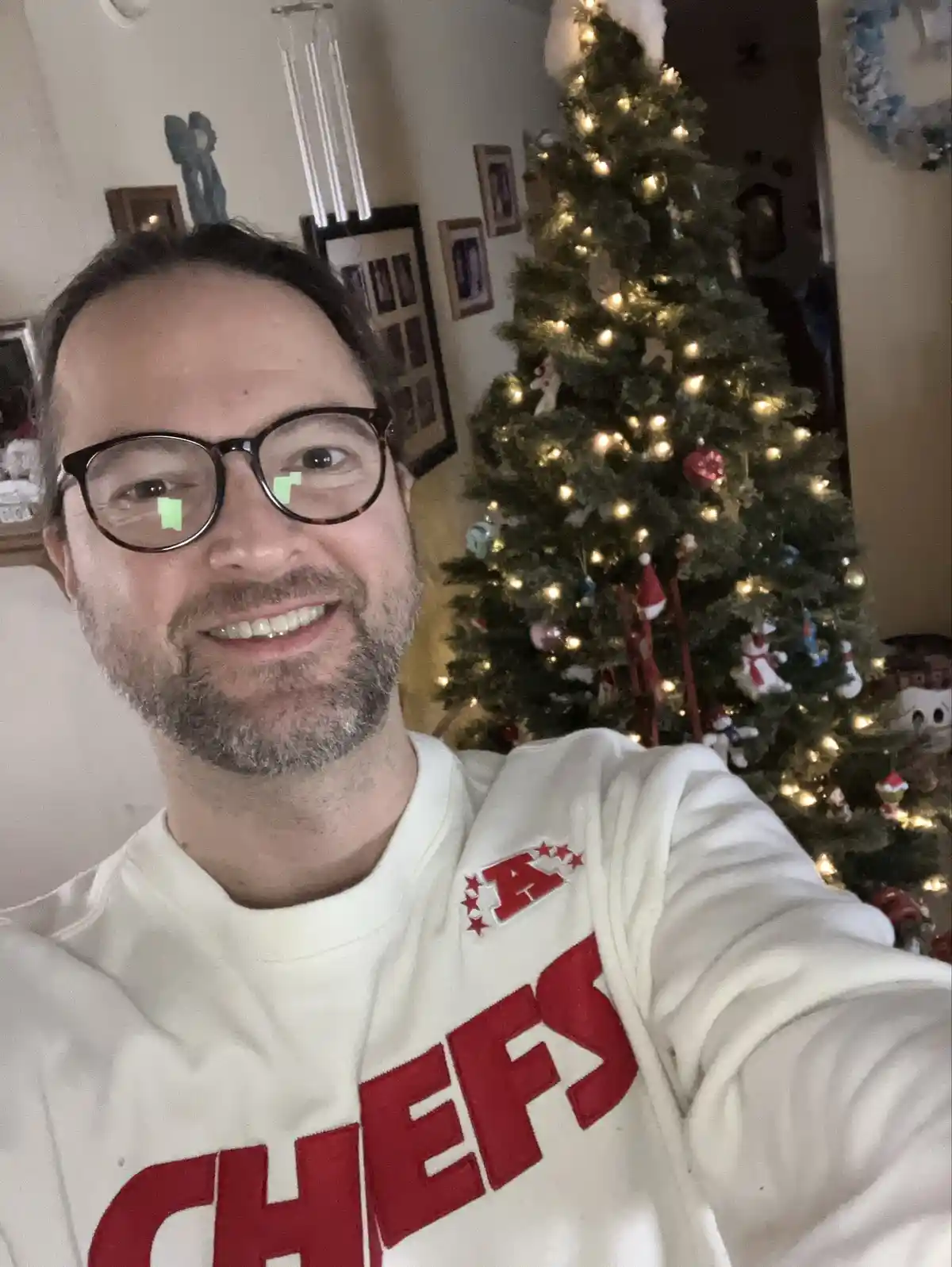 A man with glasses and a beard smiles at the camera while wearing a white sweatshirt with 'CHEFS' in red letters. Behind him…