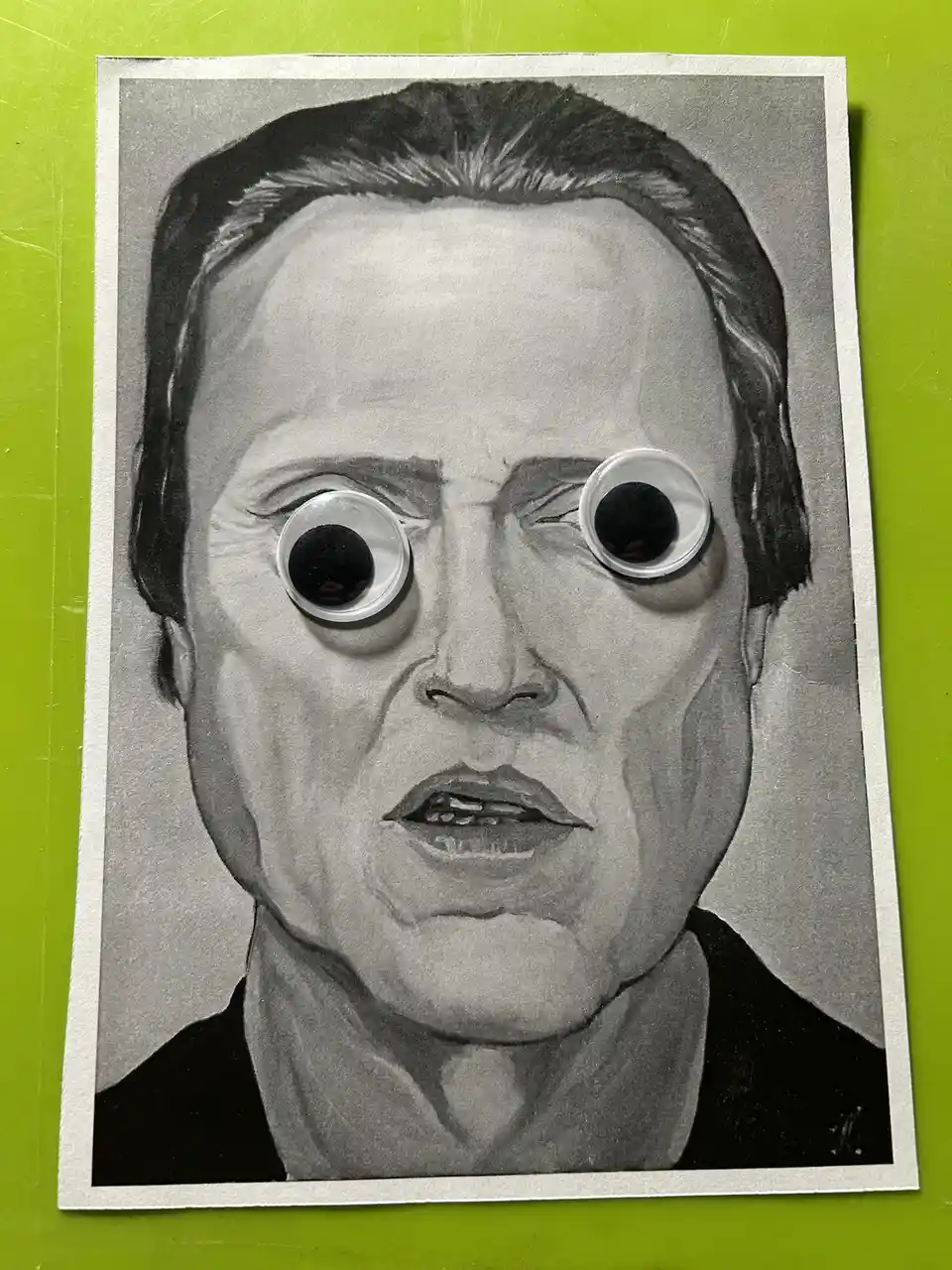 A black-and-white pencil drawing of a man with a shocked expression, featuring large, googly eyes pasted over his original…