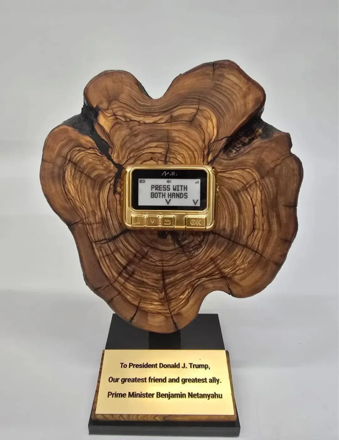 A wooden trophy with a gold-colored, retro-style electronic device embedded in its center, displaying the text 'PRESS WITH…