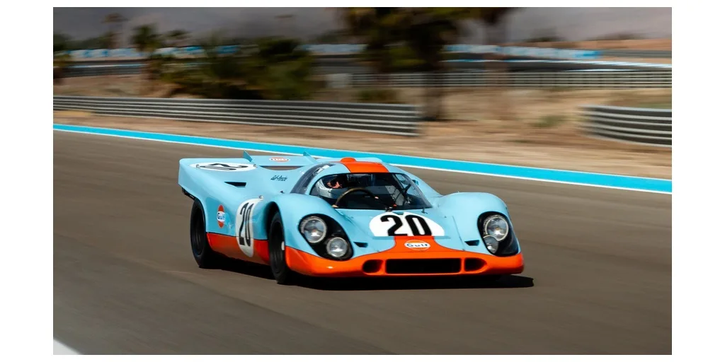 A light blue and orange vintage race car with the number 20 prominently displayed on its side and front, speeding along a…