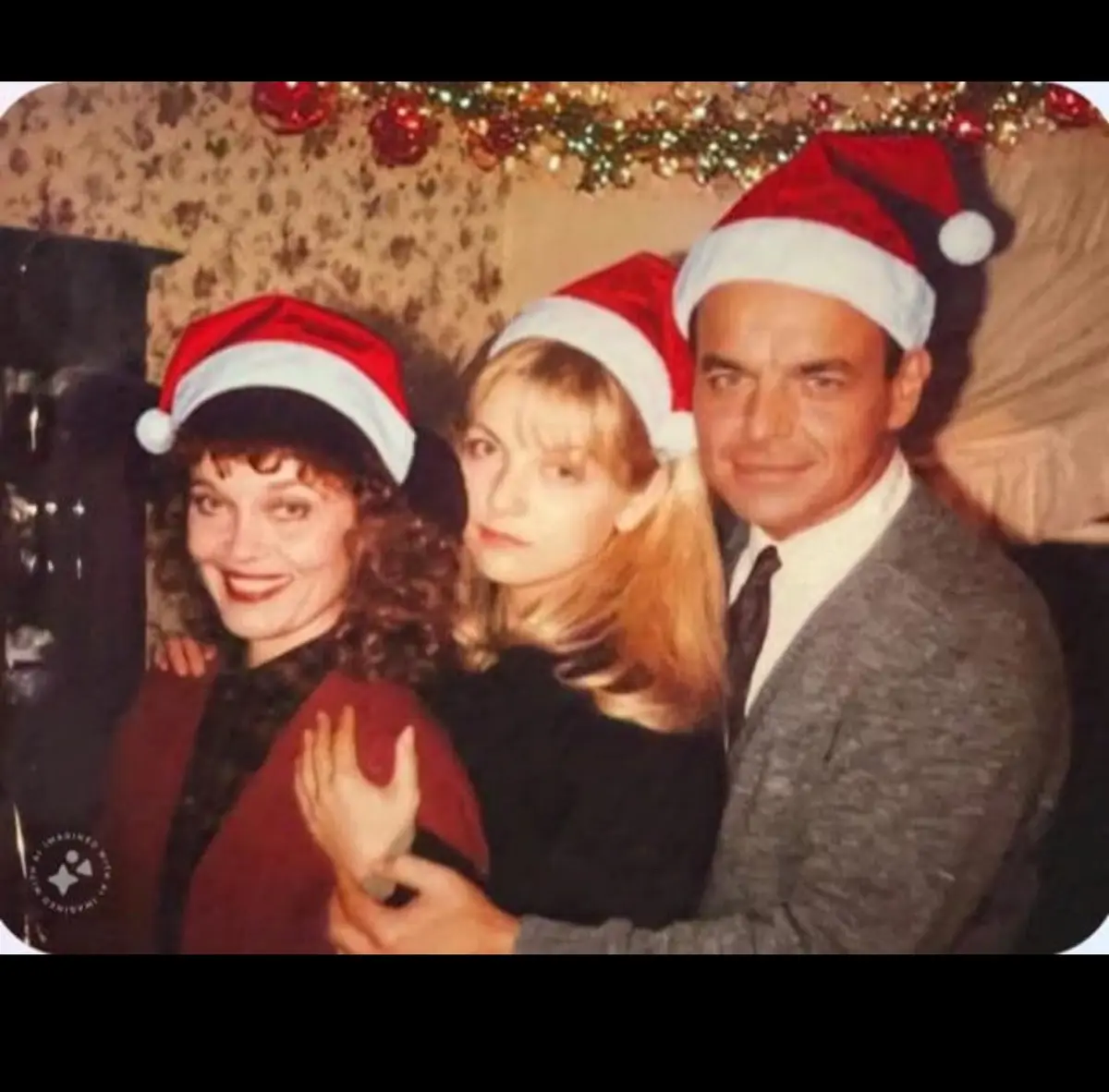 Three people wearing red and white Santa hats pose for a photo in a festively decorated room with Christmas garland above…
