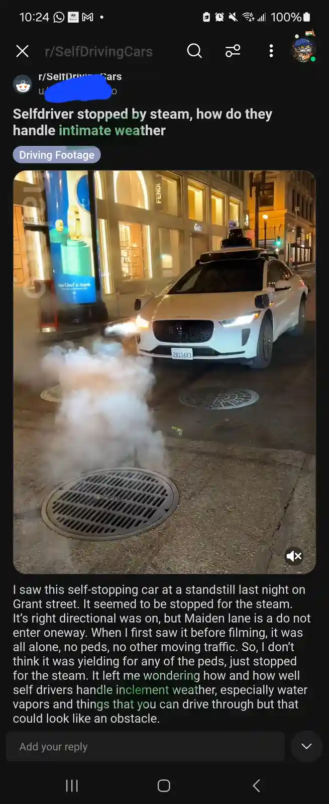A white self-driving car is stopped on a city street at night, directly in front of a plume of steam rising from a manhole…