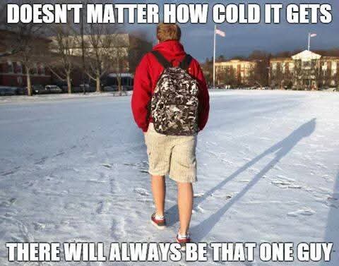 A person wearing a red jacket, shorts, and a backpack walks away from the camera across a snowy field. The sky is clear and…