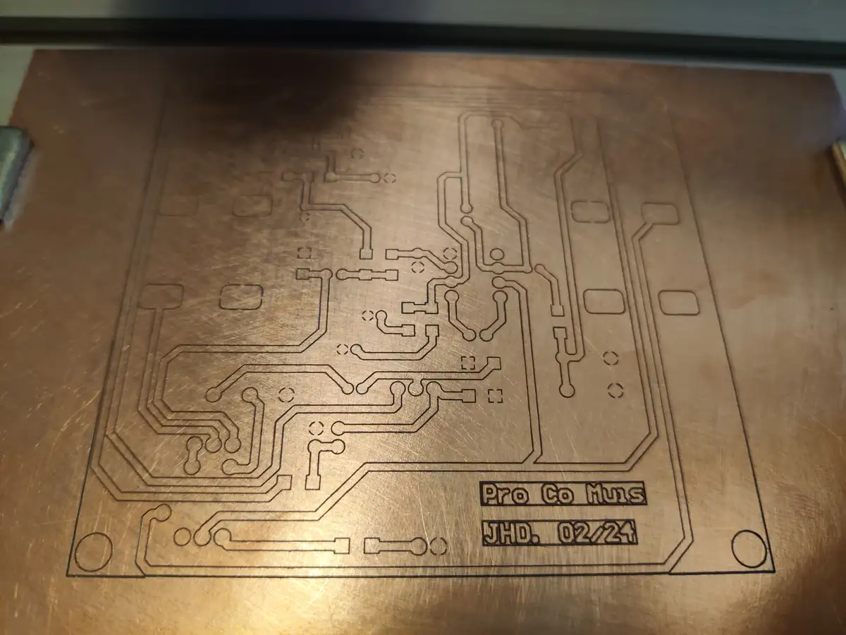A close-up of a metal plate with etched circuit board patterns resembling a PCB layout, featuring text in the bottom right…