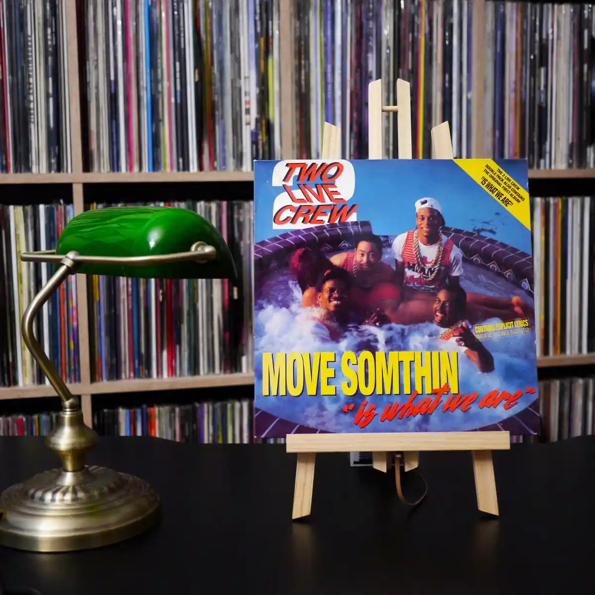 A vintage album cover for 'Two Live Crew' titled 'Move Somthin' is displayed on a small wooden easel. The cover features…