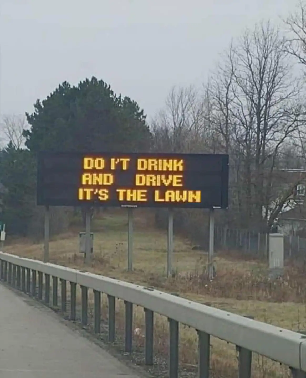A roadside electronic sign displays the message 'DO I'T DRINK AND DRIVE IT'S THE LAWN' in bright yellow letters against a…