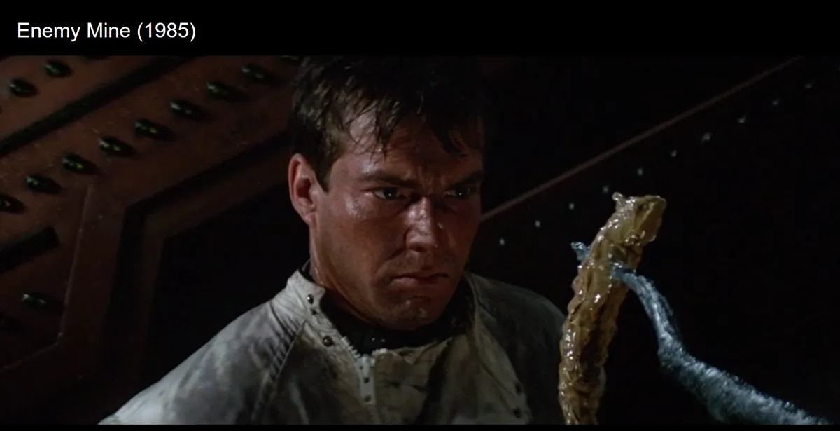 A close-up of a man in a dirty jacket looking intensely at a slimy, alien-looking object he's holding, with the text 'Enemy…