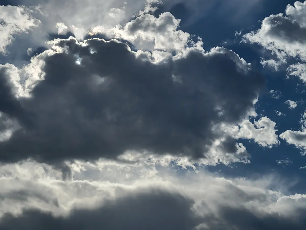 A dramatic sky photo shows a large, dark, ominous cloud dominating the center against a deep blue sky with sunbeams breaking…
