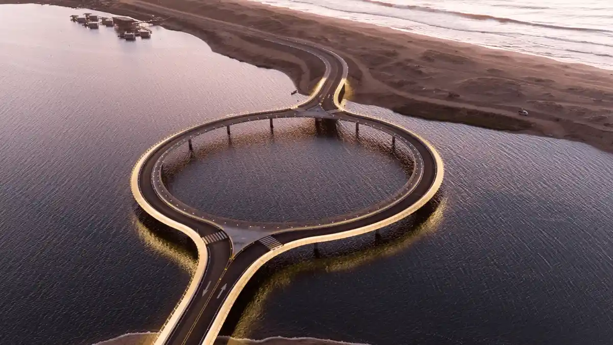 An aerial view shows a strikingly curved, circular road built over water, connecting to a sandy beach and ocean. The road…
