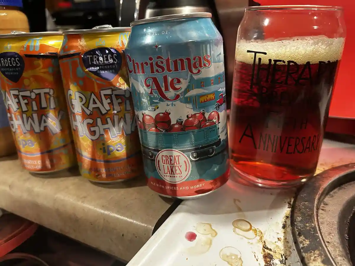 Three beer cans and a glass sit on a kitchen counter. Two orange Troegs 'Graffiti Highway' IPAs, a blue Great Lakes…