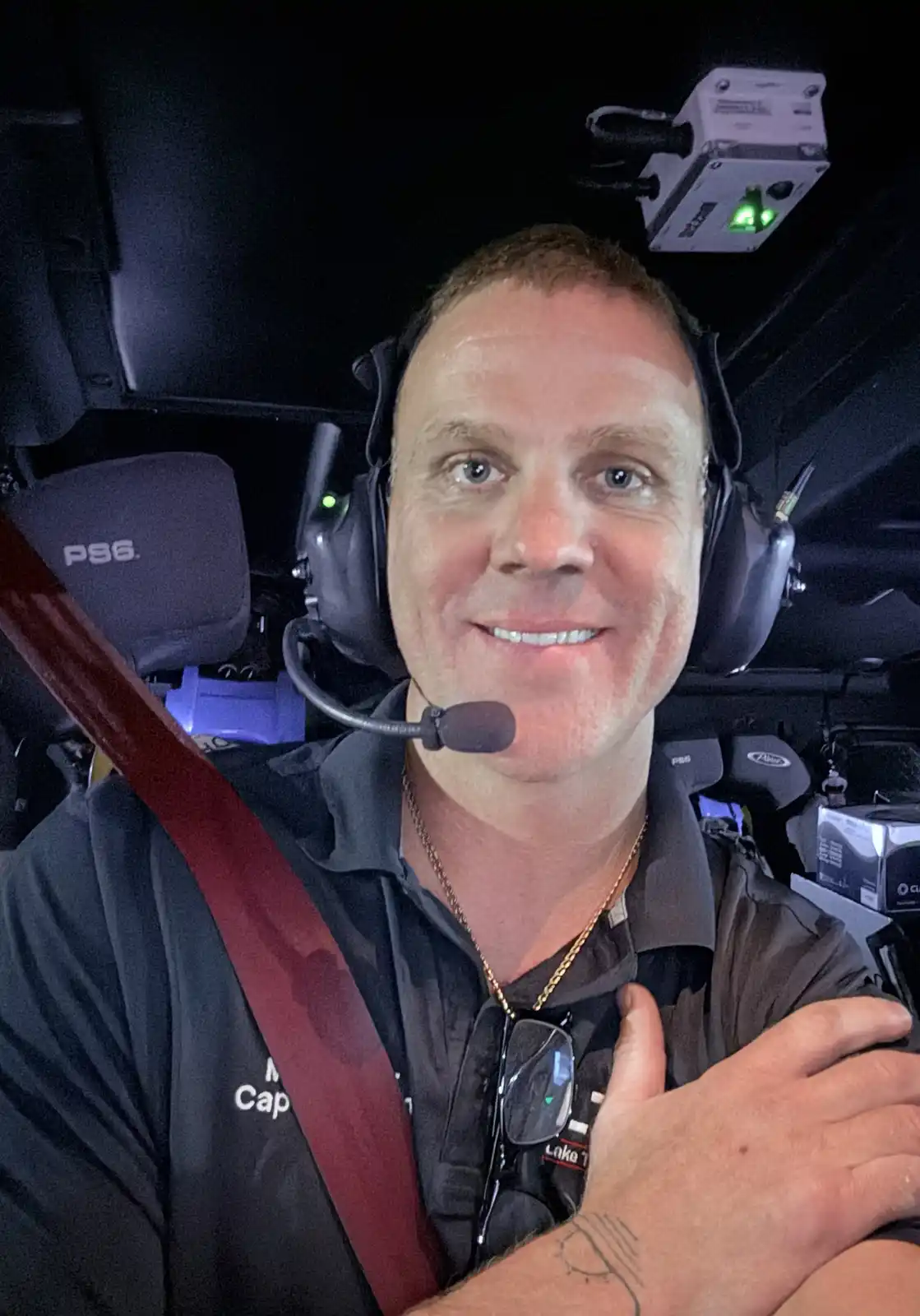 A man wearing a headset and a dark shirt with 'Captain' partially visible on it, sitting in what appears to be a boat or…