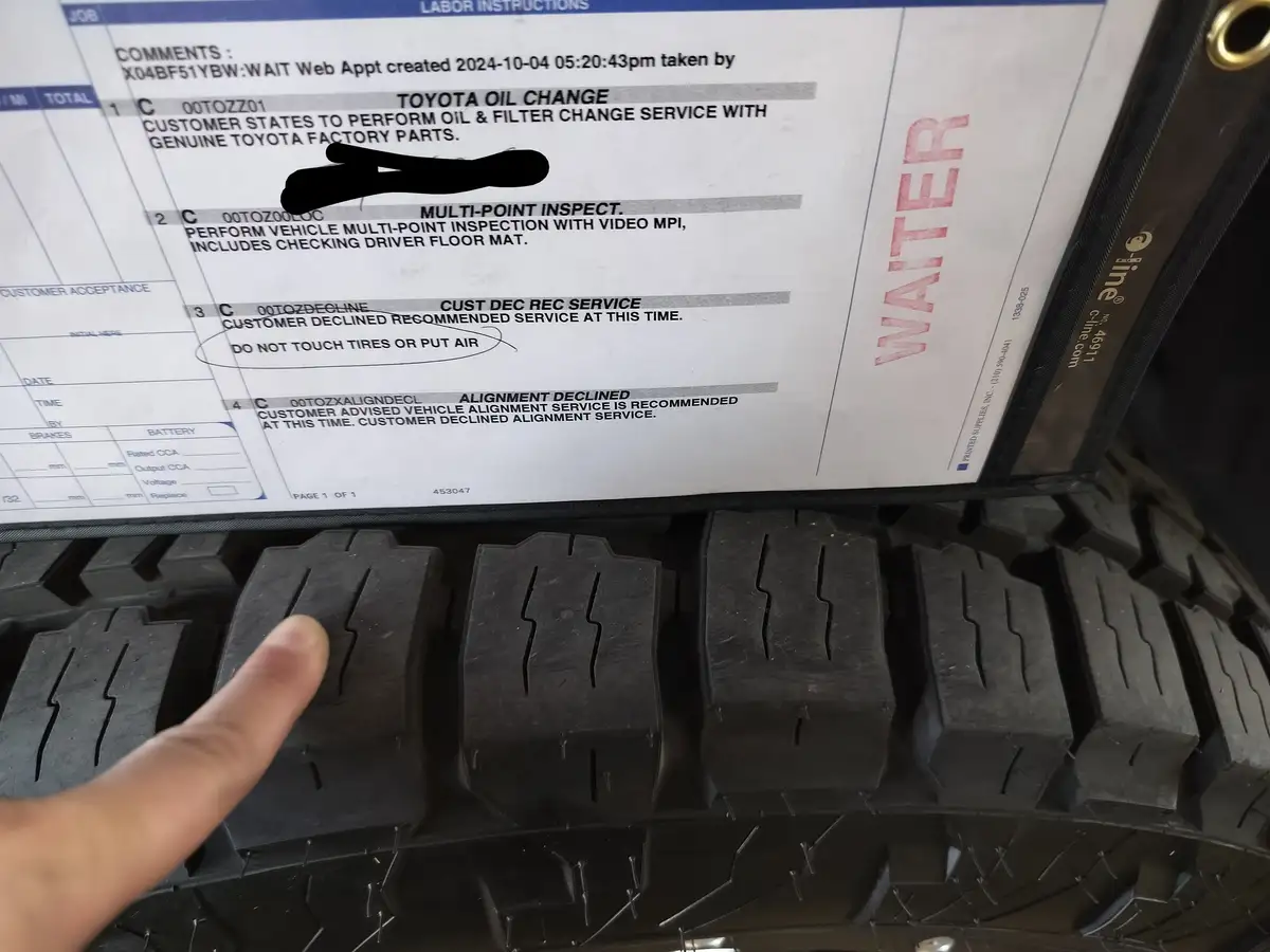 A close-up photo shows a finger pointing at a tire tread pattern, with a vehicle service labor sheet visible above. The…