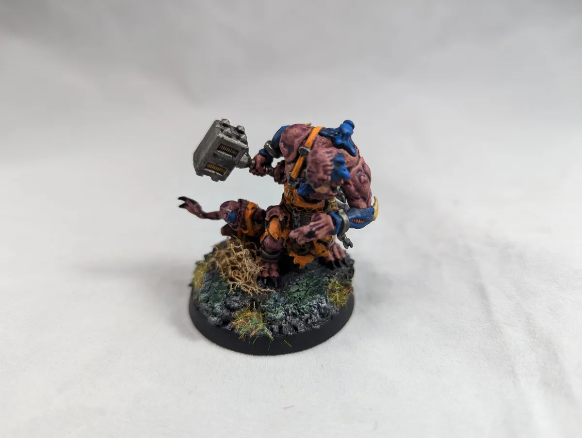 A painted miniature of a large, muscular, purple-skinned fantasy creature with blue armor and orange straps, wielding a…