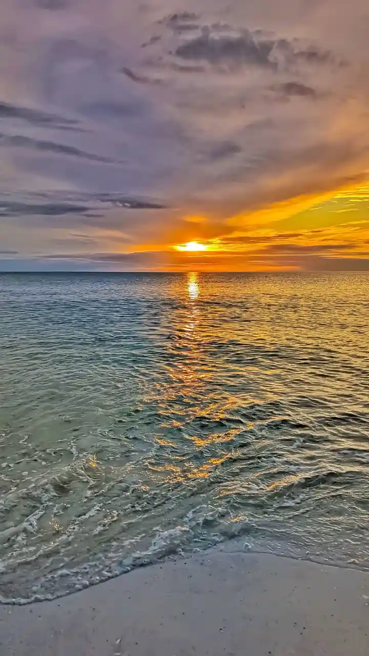 A serene sunset over the ocean with the sun low on the horizon, casting a golden reflection across the water. The sky is…