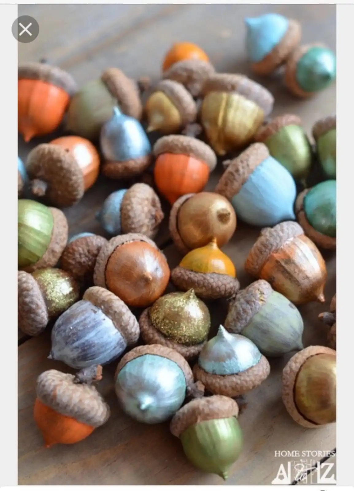 A pile of acorns with their natural caps, each painted in various metallic and pastel colors like gold, blue, green, and…