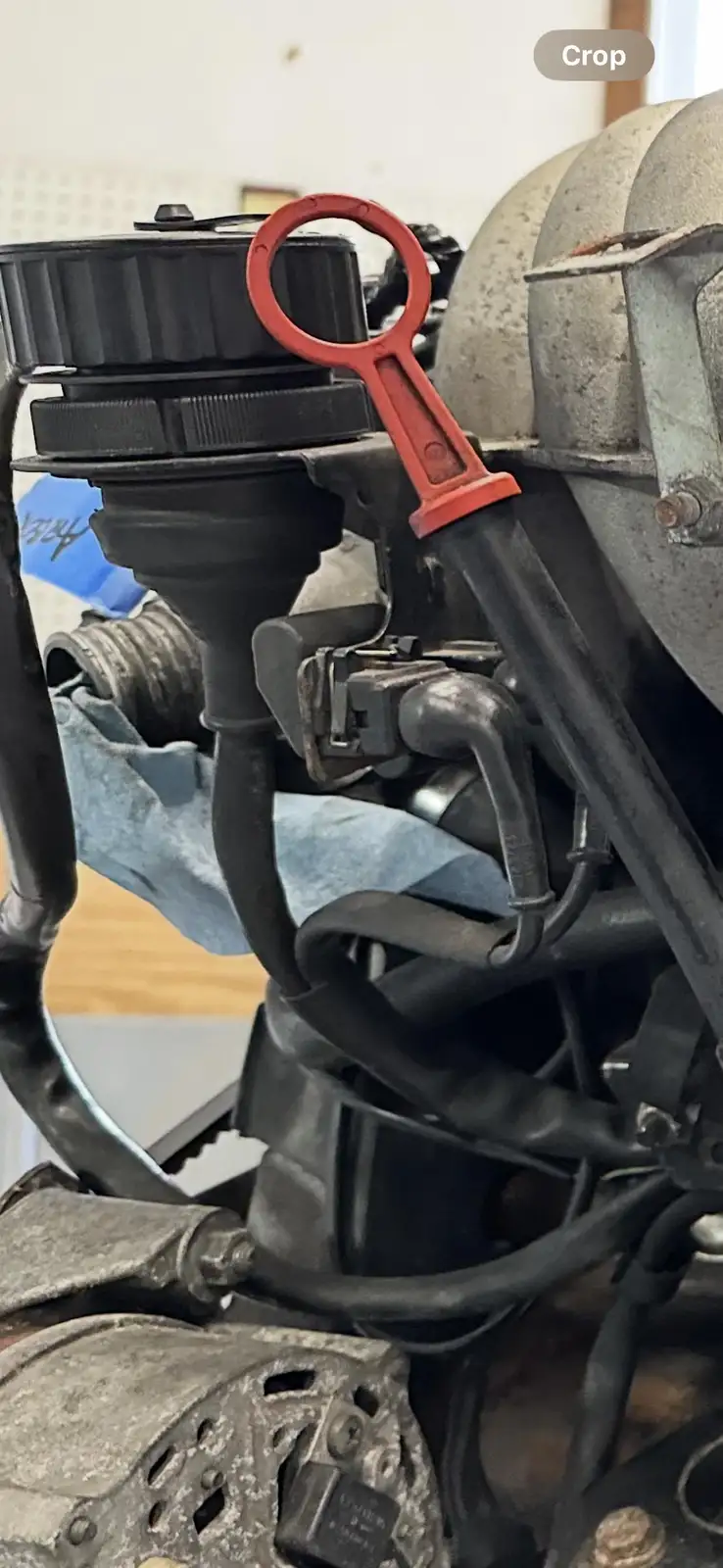 A close-up photo of a car engine with a red plastic tool shaped like a key inserted into a black cap. The overlaid text…