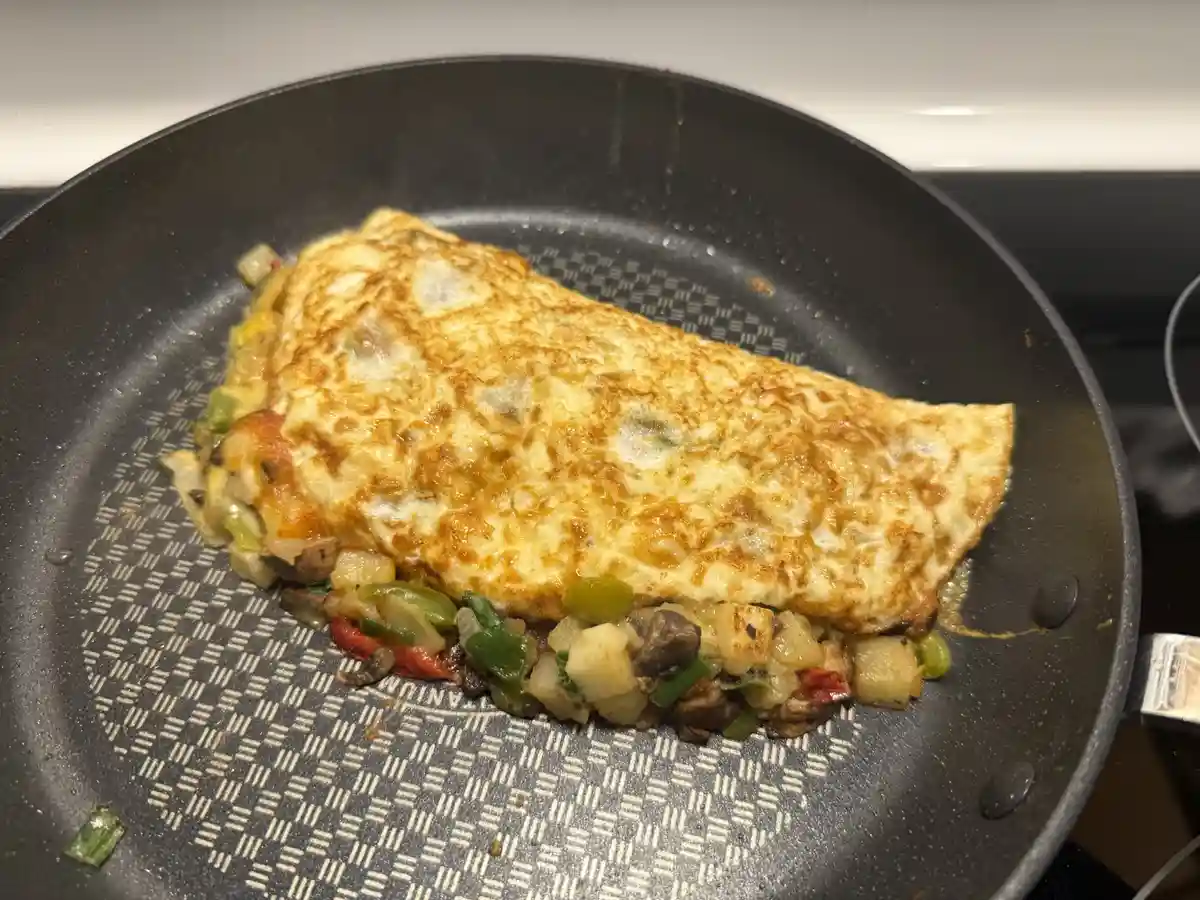 A close-up photo shows a golden-brown omelette folded over a bed of colorful sautéed vegetables like peppers, onions, and…
