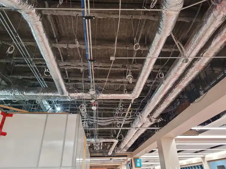 The image shows a ceiling with exposed ductwork, wires, and structural elements, resembling an unfinished or poorly…
