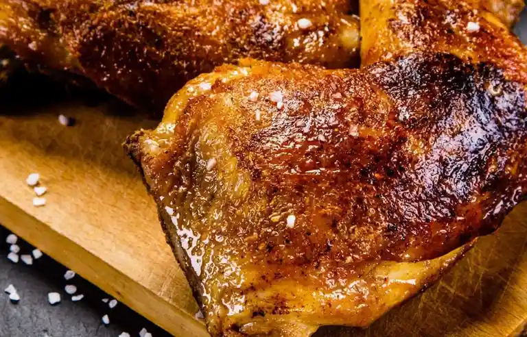 A close-up photo of golden-brown, crispy roasted chicken wings with coarse salt sprinkled on top, resting on a wooden…