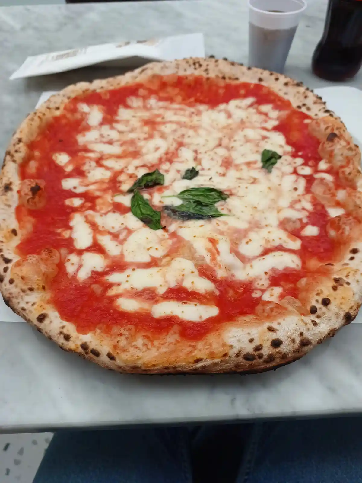 A close-up photo of a freshly baked margherita pizza on a marble table, featuring a charred crust, red tomato sauce, melted…