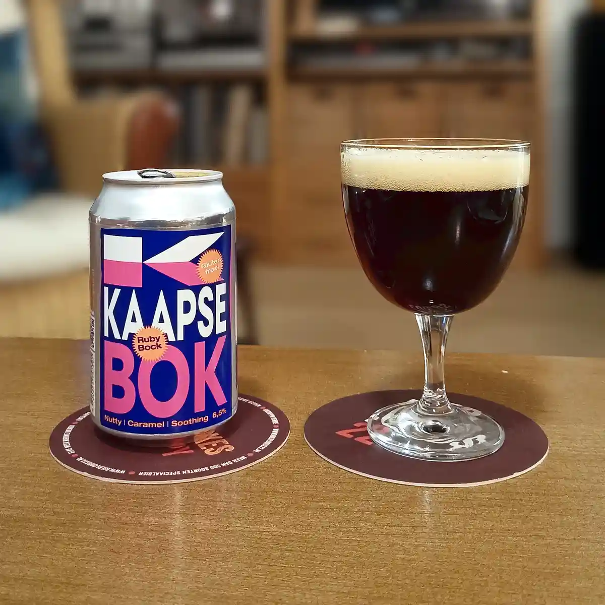 A silver can of Kaapse Bok Ruby Bock beer, labeled 'Gluten free!' and 'Nutty | Caramel | Soothing 6,5%', sits next to a…