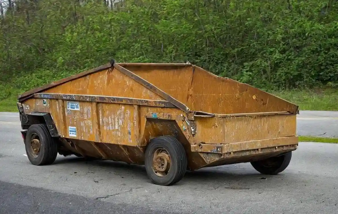 a rusty, weathered dump truck is parked on a paved road with a forested area behind it. The truck's body is heavily corroded…