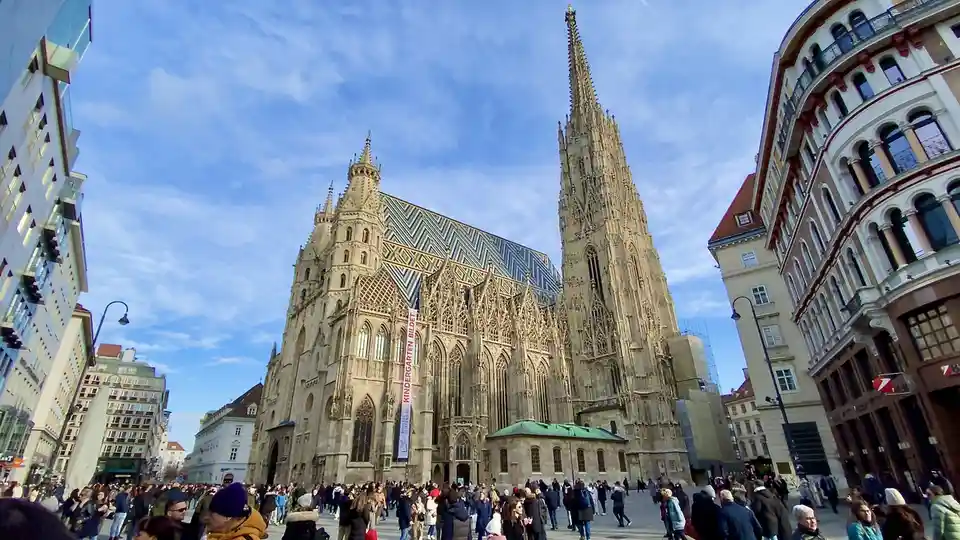 A wide-angle photo shows the ornate St. Stephen's Cathedral in Vienna, with its distinctive tiled roof and tall spire…