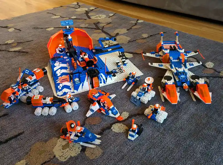 A large, elaborate LEGO space-themed set, featuring a central blue and orange base with an open dome, surrounded by multiple…