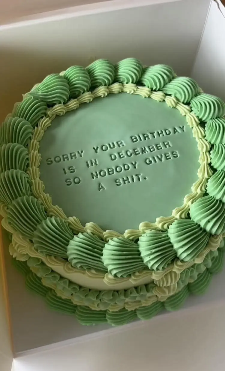 A round birthday cake with green and light green frosting, featuring piped decorative borders and embossed text in the…
