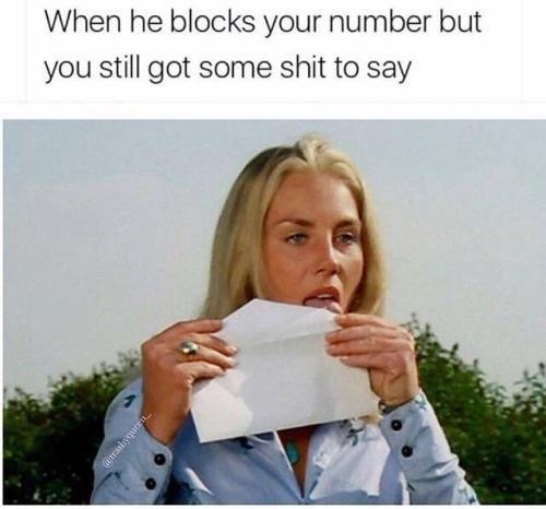 A woman with blonde hair, wearing a light blue button-up shirt, holds a white envelope to her mouth as if about to speak or…