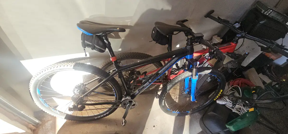 A black and blue mountain bike with a red bike behind it is parked in a cluttered garage, with the overlaid text 'i bought a…