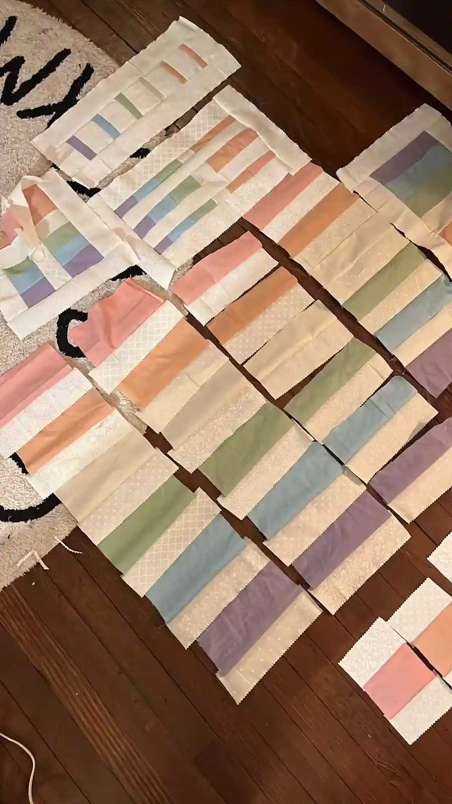 An overhead shot shows numerous rectangular fabric pieces, each with pastel-colored stripes on a white background, arranged…