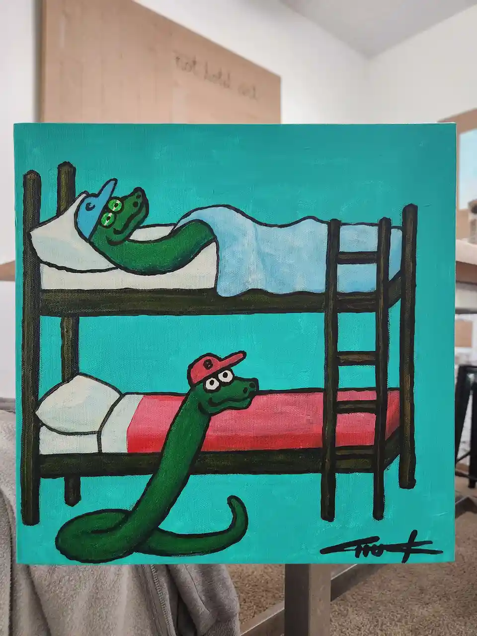 A hand-painted canvas depicts two green cartoon snakes in bunk beds; the top snake wears a blue hat and sleeps under a blue…