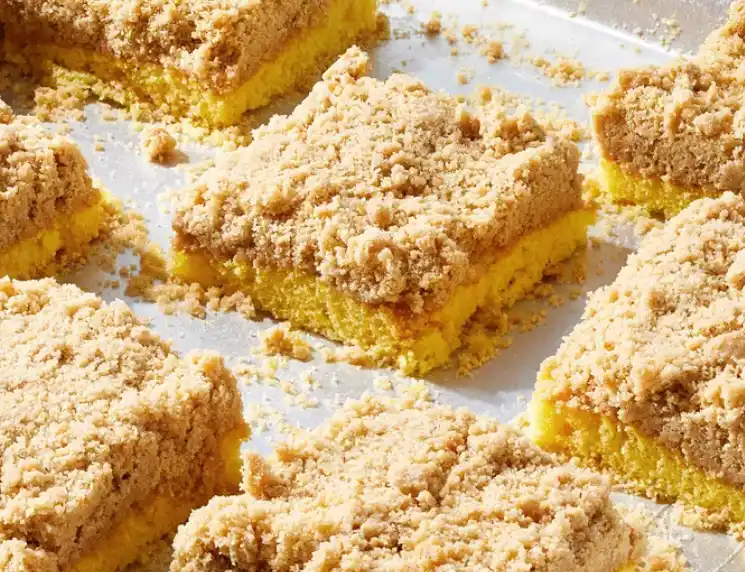A close-up photo of square yellow cake bars with a crumbly, brown sugar topping, arranged on a baking sheet. Overlaid text…