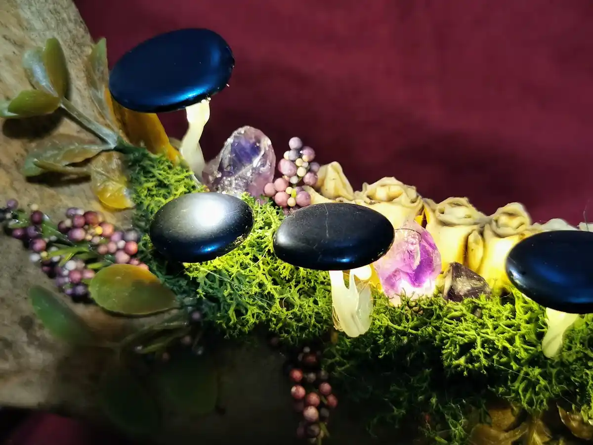 A close-up photo of decorative mushrooms with shiny black caps and white stems, arranged on green moss alongside purple…