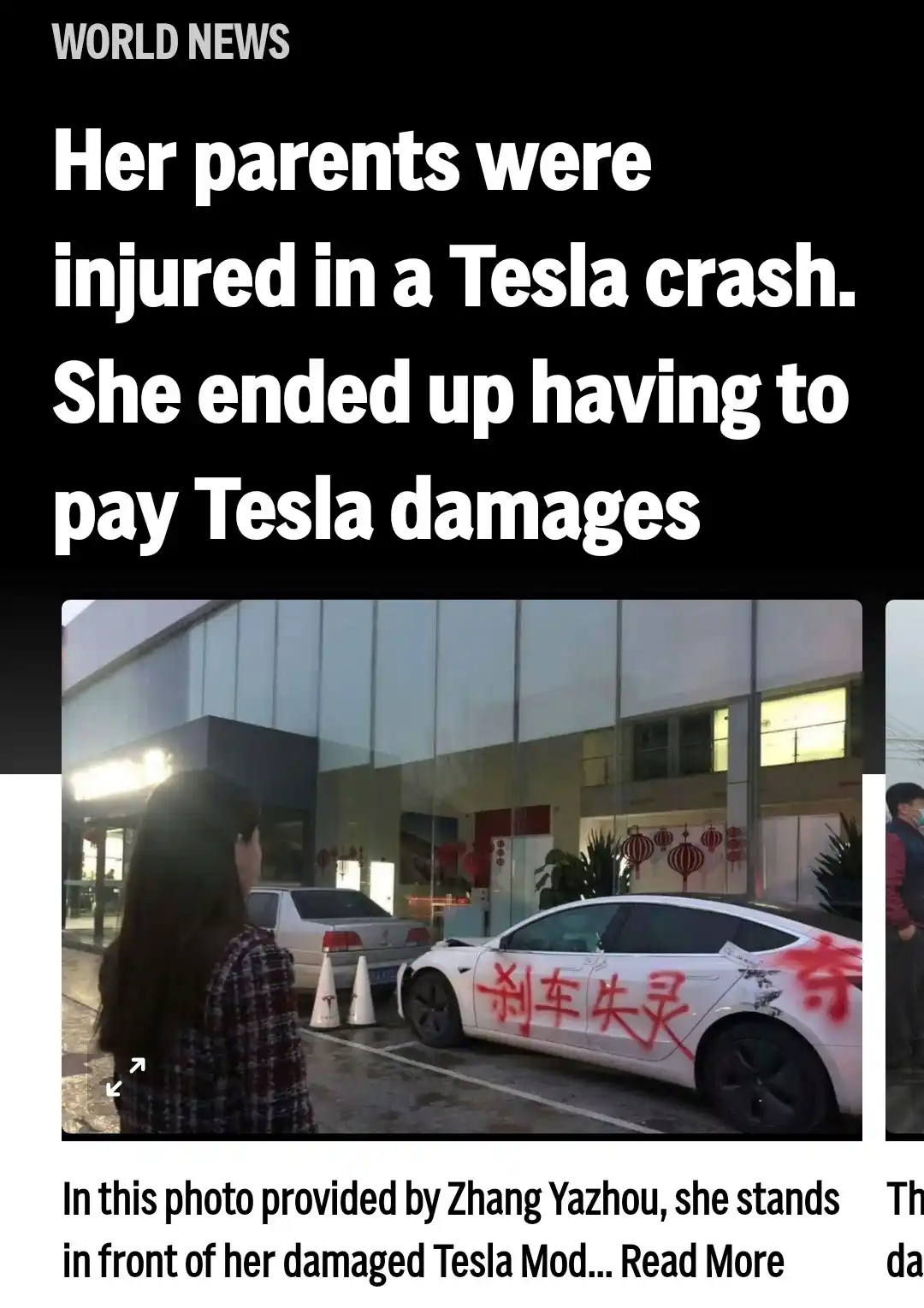 A woman stands in front of a damaged white Tesla Model S with red Chinese characters spray-painted on its side. The car is…