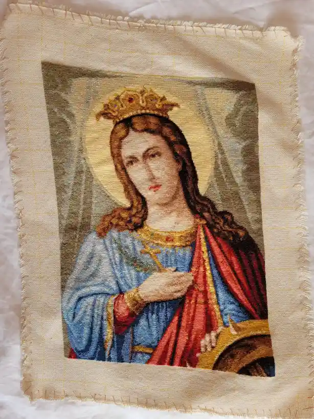 A close-up of a needlepoint tapestry depicting a crowned religious figure, likely the Virgin Mary, wearing a blue robe with…