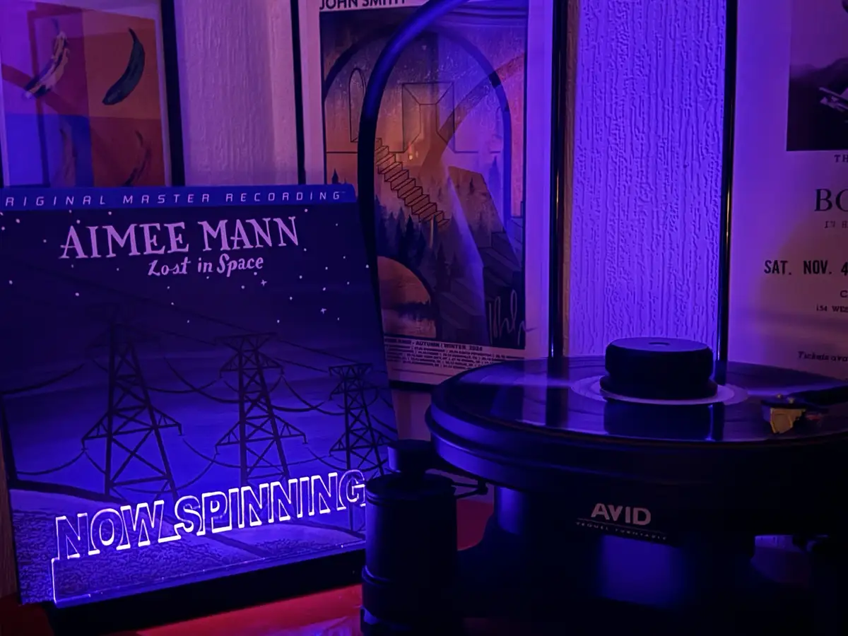 A vinyl record player with a record on it sits next to a glowing album cover for Aimee Mann's 'Lost in Space'. The album…