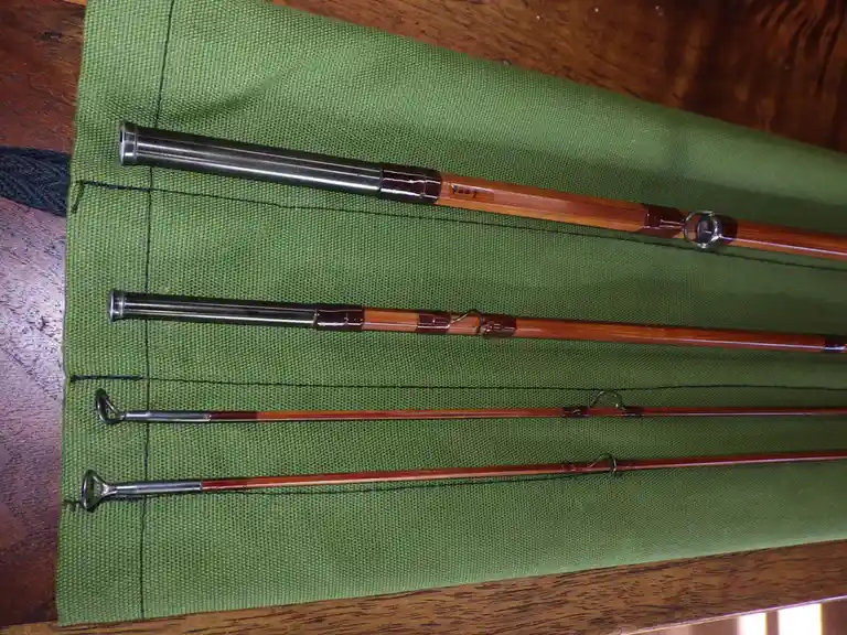 Four segmented bamboo fishing rods with metal ferrules lie neatly arranged on a green fabric mat atop a wooden table. The…