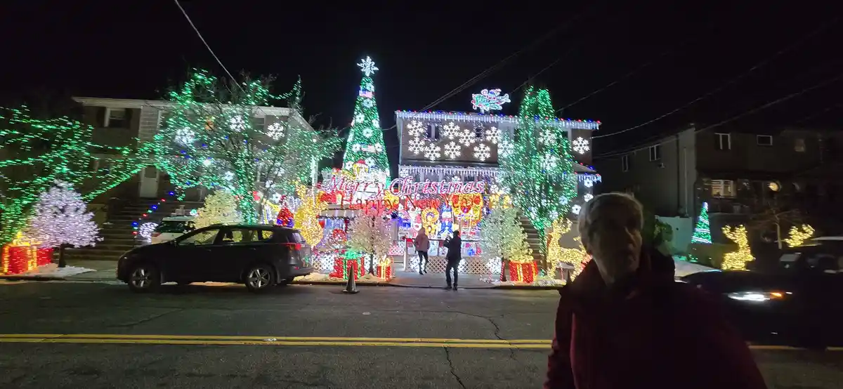 A nighttime street scene features a house extravagantly decorated with bright Christmas lights, including a large tree…