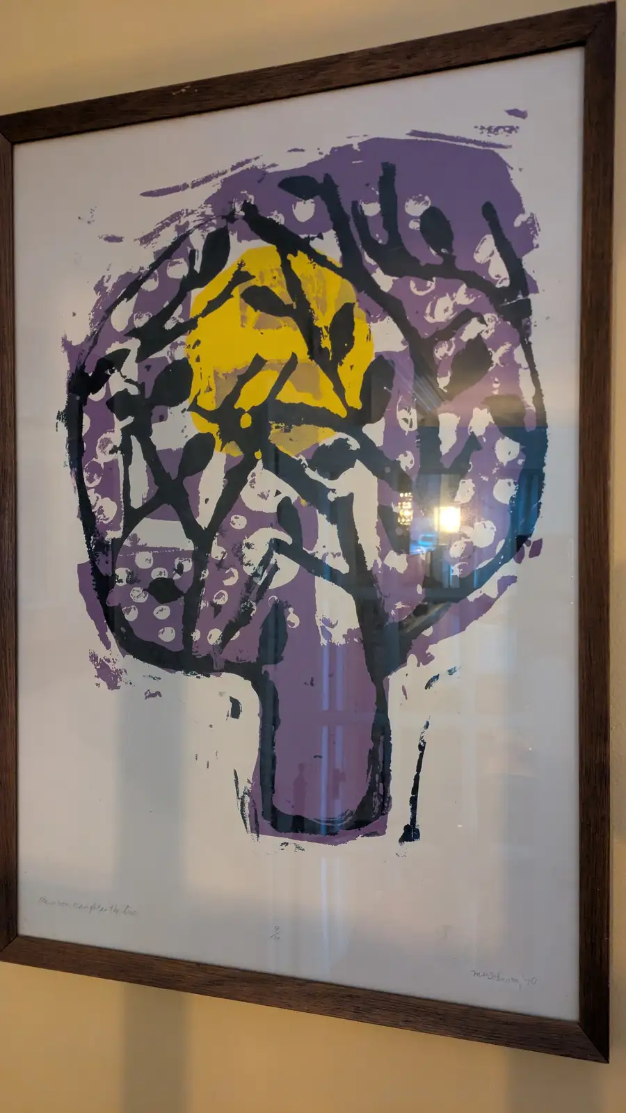 A framed abstract print shows a stylized tree with a yellow circular shape resembling a moon at its center, surrounded by…