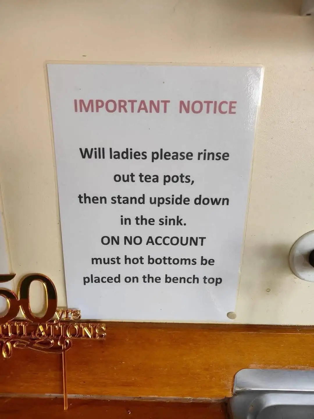 A white sign with red and black text is taped to a beige wall above a wooden counter. The sign reads 'IMPORTANT NOTICE'…