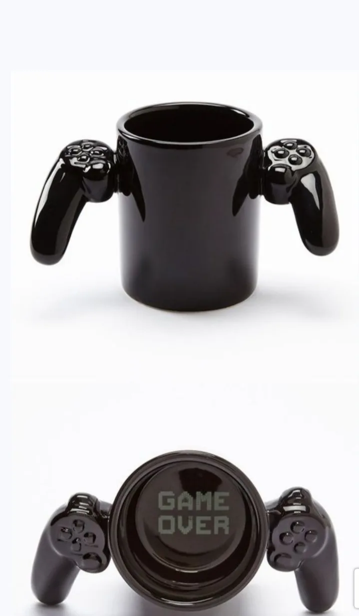A black ceramic mug shaped like a video game controller with handles on each side, shown from the front and then flipped…