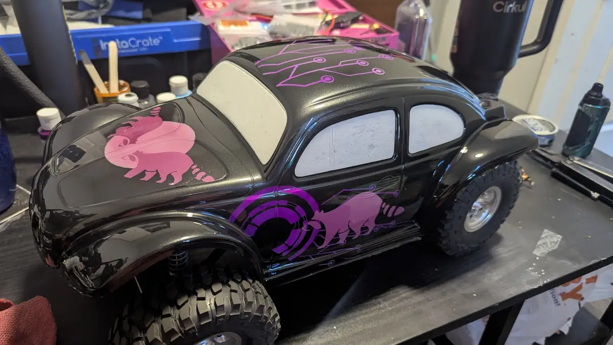 A black remote-controlled Volkswagen Beetle model with pink and purple decals of cartoon bears and circuit board patterns…