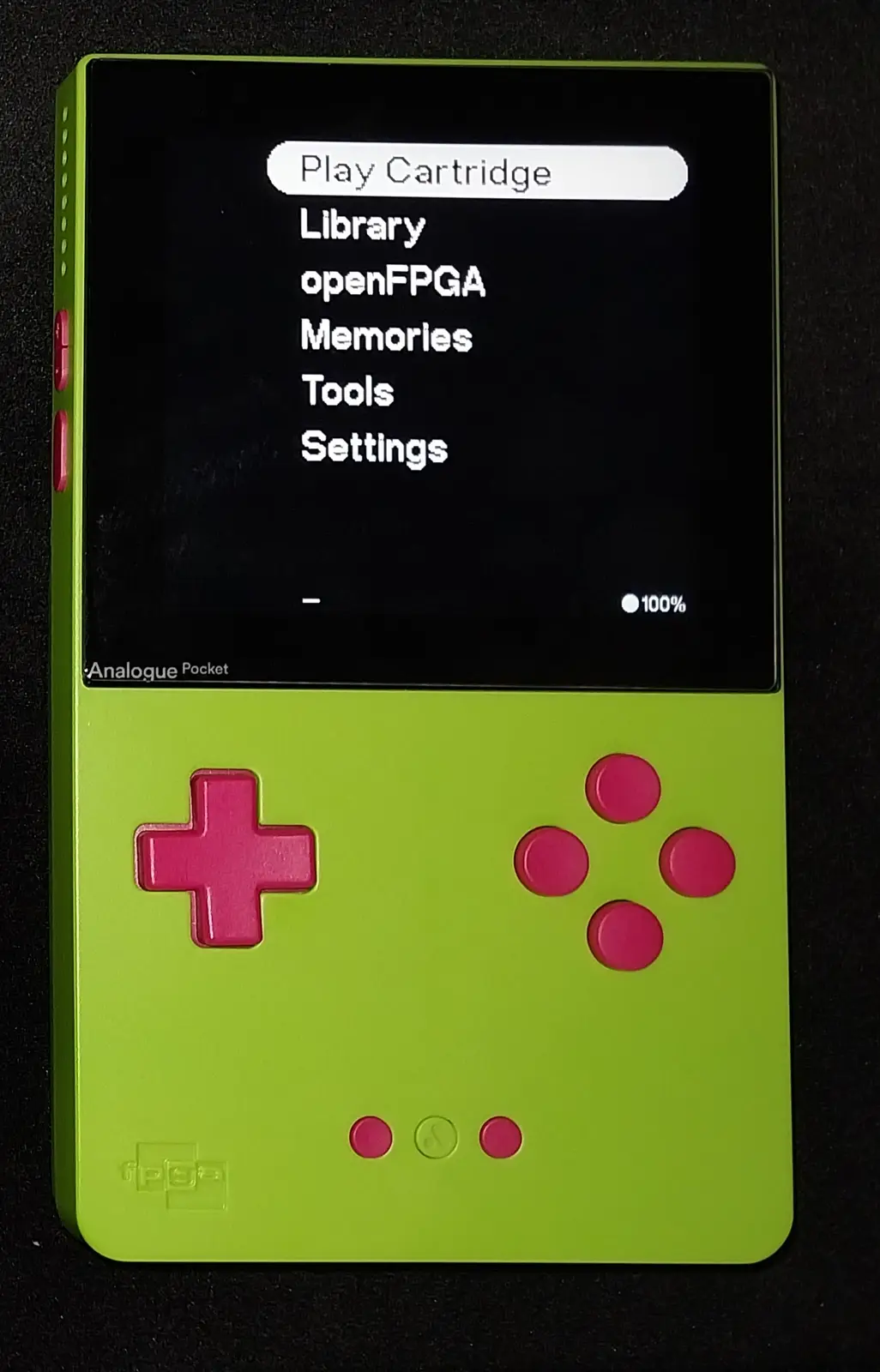 A lime green handheld gaming device, resembling a Game Boy, displays a menu with options including 'Play Cartridge'…