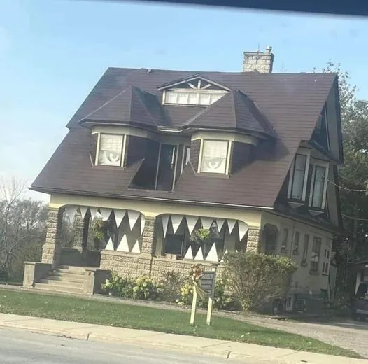 a photo of a large, ornate, two-story house with a dark roof and stone foundation, decorated with white triangular bunting…