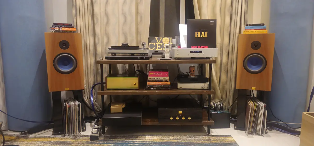 A high-end home audio setup featuring two large wooden floor-standing speakers with blue woofers, a multi-tiered wooden…