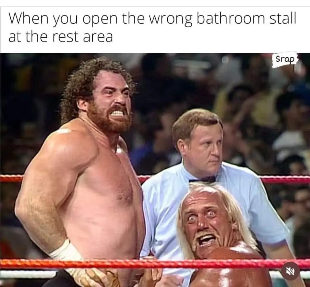 A shirtless, muscular wrestler with curly hair and a beard stands in a wrestling ring, glaring intensely with his teeth…